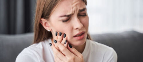 image of young women suffering from toothache while sitting on the sofa at home.